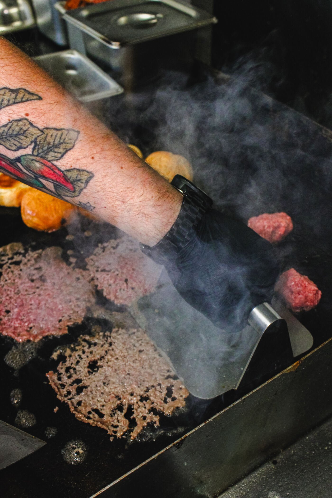 Hand-rolled beef patty being smashed on the flat-top grill